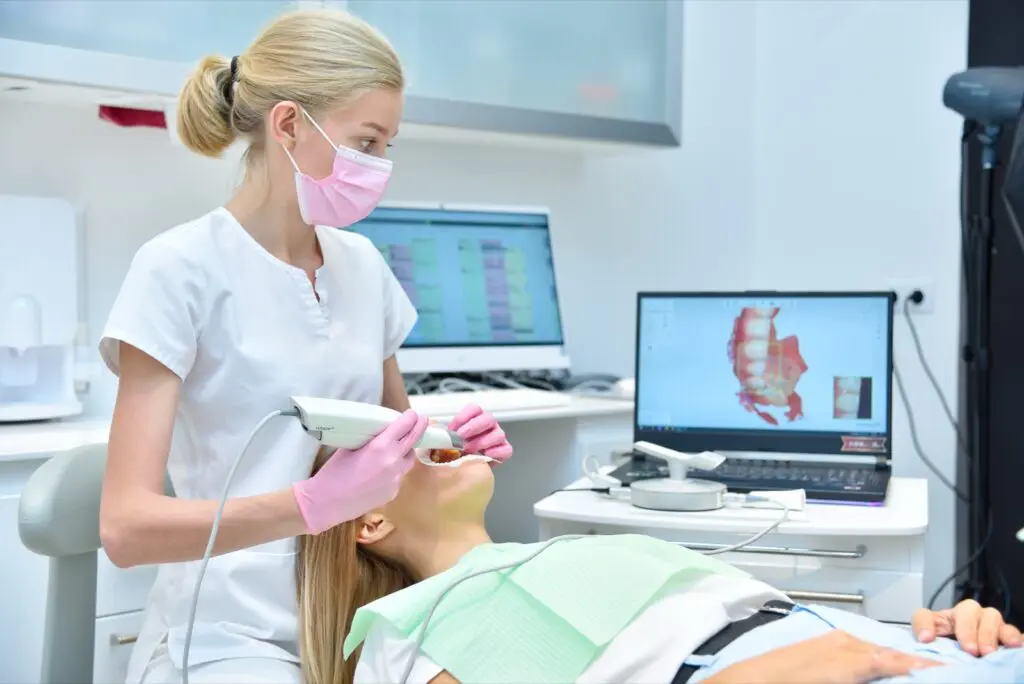 Denturist scanning patient with dental intraoral scanner and controls process on laptop screen. Prosthodontics and stomatology concept.