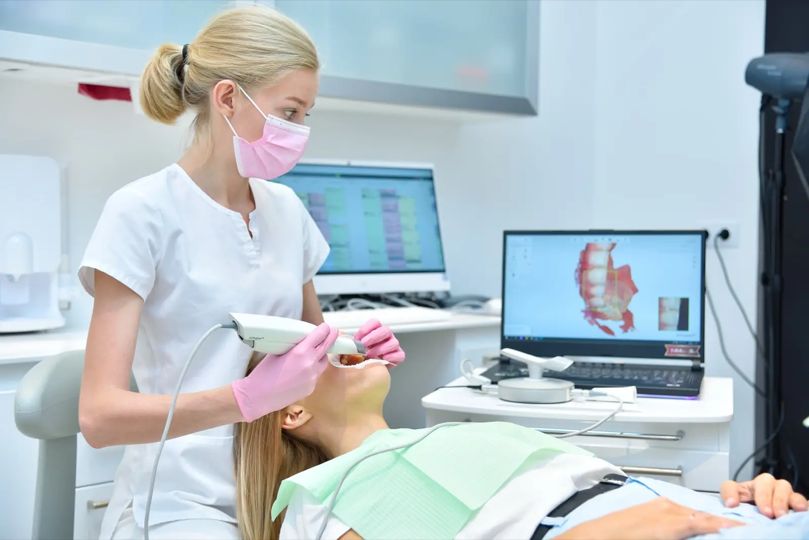 Denturist scanning patient with dental intraoral scanner and controls process on laptop screen. Prosthodontics and stomatology concept.