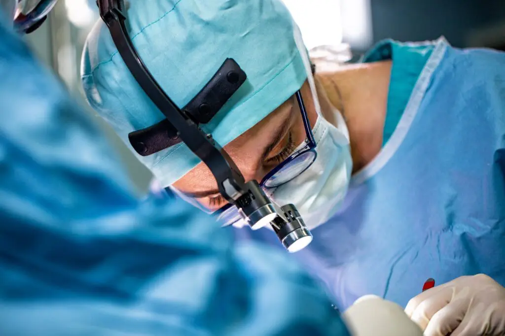 Surgeon performing surgery in hospital operating room. Surgeon in mask wearing loupes during medical procadure. Breast augmentation, enlargement, enhancement