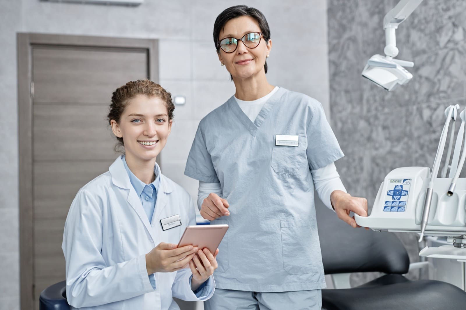 Waist up portrait of female dentist with assistant in dental clinic smiling at camera