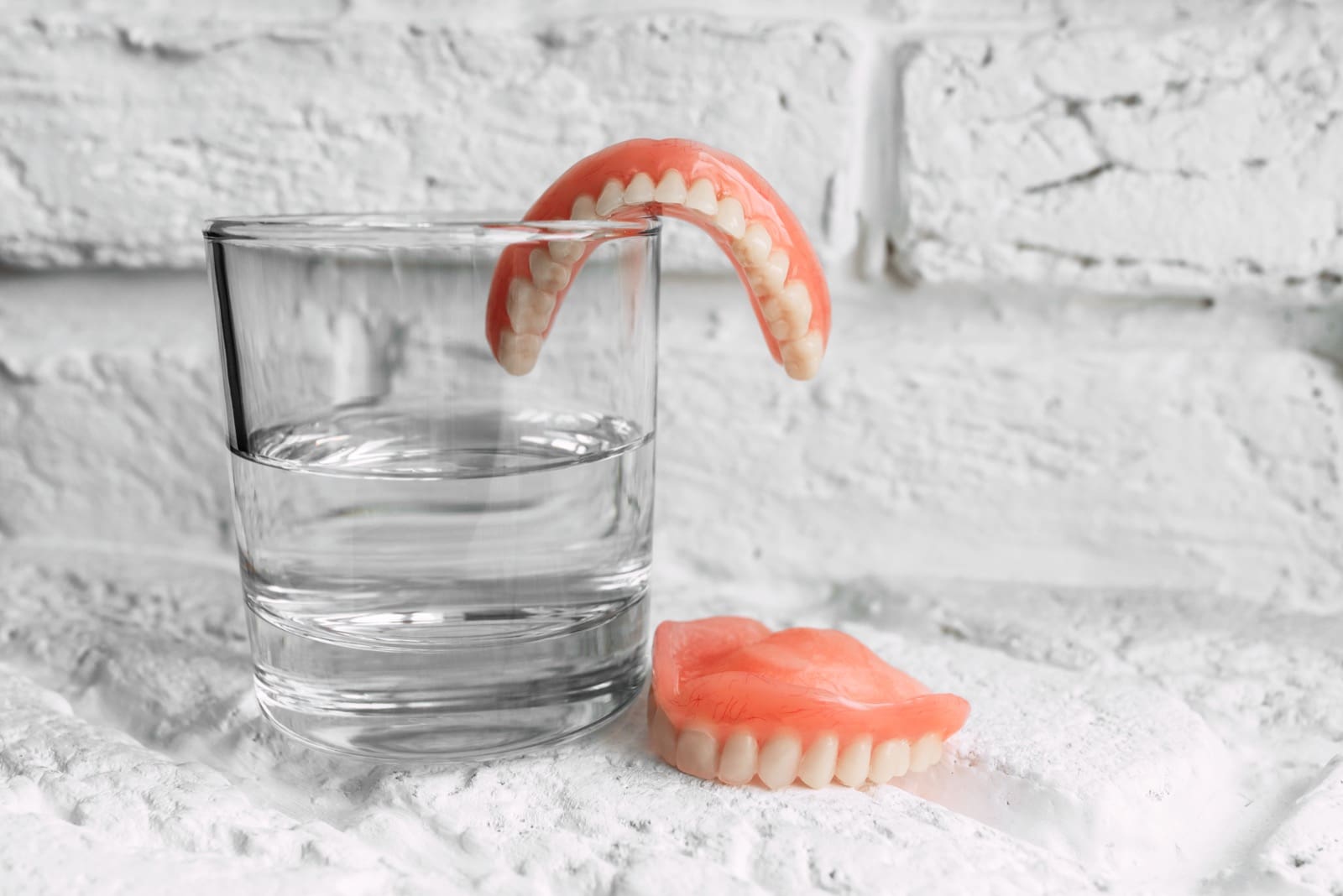A denture in a glass of water. Dental prosthesis care. Full removable plastic denture of the jaws. Two acrylic dentures. Upper and lower jaws with fake teeth. Dentures or false teeth, close-up.