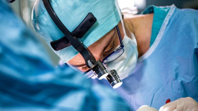Surgeon performing surgery in hospital operating room. Surgeon in mask wearing loupes during medical procadure. Breast augmentation, enlargement, enhancement